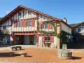 Maison basque traditionnelle à colombages rouges et blancs, avec un puits ancien devant. Un lieu plein de charme à Saint-Pée-sur-Nivelle.