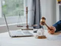 Marteau de juge frappant une maison miniature, symbolisant la loi Carrez pour une maison individuelle. Balance de la justice et ordinateur en arrière-plan.