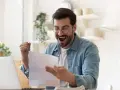 Homme joyeux, poing levé, découvrant une bonne nouvelle sur un document, peut-être la rémunération gérant SCI.