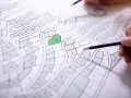 Plan cadastral de Privas, avec une parcelle verte mise en évidence. Des mains tiennent des crayons, prêtes à annoter.