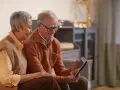 Un couple âgé regarde une tablette, peut-on louer un appartement après 70 ans ? Ils semblent heureux de leurs recherches.