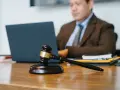 Marteau de juge sur un bureau, avec un homme en costume travaillant sur un ordinateur portable en arrière-plan. Explication de l'article 1722 du Code civil.