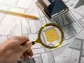 Une loupe examine un plan de cadastre d'Aix, révélant la parcelle 220. Un crayon et une maquette de maison sont posés sur les plans.