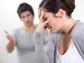 Couple en conflit, femme se tenant le front, homme parlant au fond.