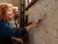 Un couple peint un mur en brique, résolvant un désaccord sur les travaux en indivision avec bonne humeur.