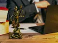 Statue de la justice, livres, ordinateur portable et stylo sur un bureau en bois. Un avocat examine les frais de donation.