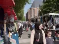 Ambiance de marché animé à **Plu Roubaix**, avec des étals de vêtements colorés et des passants sous le soleil.