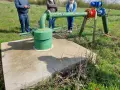 Installation de forage agricole, respectant la réglementation. Des personnes observent le système de pompage et de tuyauterie verte et bleue.