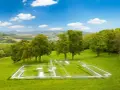 Plan d'une maison superposé sur un terrain verdoyant, illustrant la constructibilité d'un terrain. Paysage bucolique sous un ciel bleu.