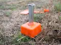 Borne orange avec un tube métallique planté dans le sol. D'autres bornes sont visibles en arrière-plan, indiquant le bornage d'un terrain déjà borné.