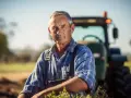 Un fermier expérimenté, son visage marqué par le soleil, pense à son **salaire différé et indivision** tout en regardant vers l'avenir, un tracteur en arrière-plan.
