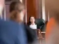Une avocate présente son dossier, le dol, devant un juge. La salle d'audience est sombre et solennelle.