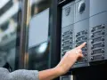 Une main appuie sur un bouton d'interphone, rappelant l'obligation du propriétaire d'assurer ce système.