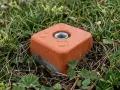 Un piquet de bornage orange, en partie enterré dans l'herbe et les petites fleurs sauvages, marque une limite discrète dans la nature.