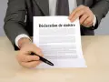 Un homme en costume gris tient un document intitulé "Déclaration de sinistre", prêt à signer.