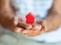 Mains âgées tenant une petite maison rouge. Une image symbolisant la "cosaisine définition" : le foyer, la sécurité, le bien-être.