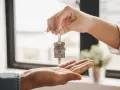 Une main tend une clé avec un pendentif en forme de maison, symbolisant une convention d'occupation anticipée avant vente.