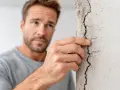 Homme inquiet examinant une fissure sur un mur, évoquant un manquement au devoir de conseil de l'agent immobilier.