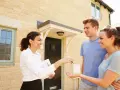 Une femme remet des clés à un jeune couple devant leur nouvelle maison. Le tableau droit de préemption locataire est respecté.