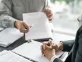 Deux personnes discutent d'un document, peut-être une clause tontine, lors d'une réunion formelle.