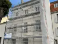 Ravalement de façade en cours, échafaudages recouvrant le bâtiment. Une bâche blanche protège une partie des travaux. L'indemnisation locataire est une préoccupation lors de ces rénovations.