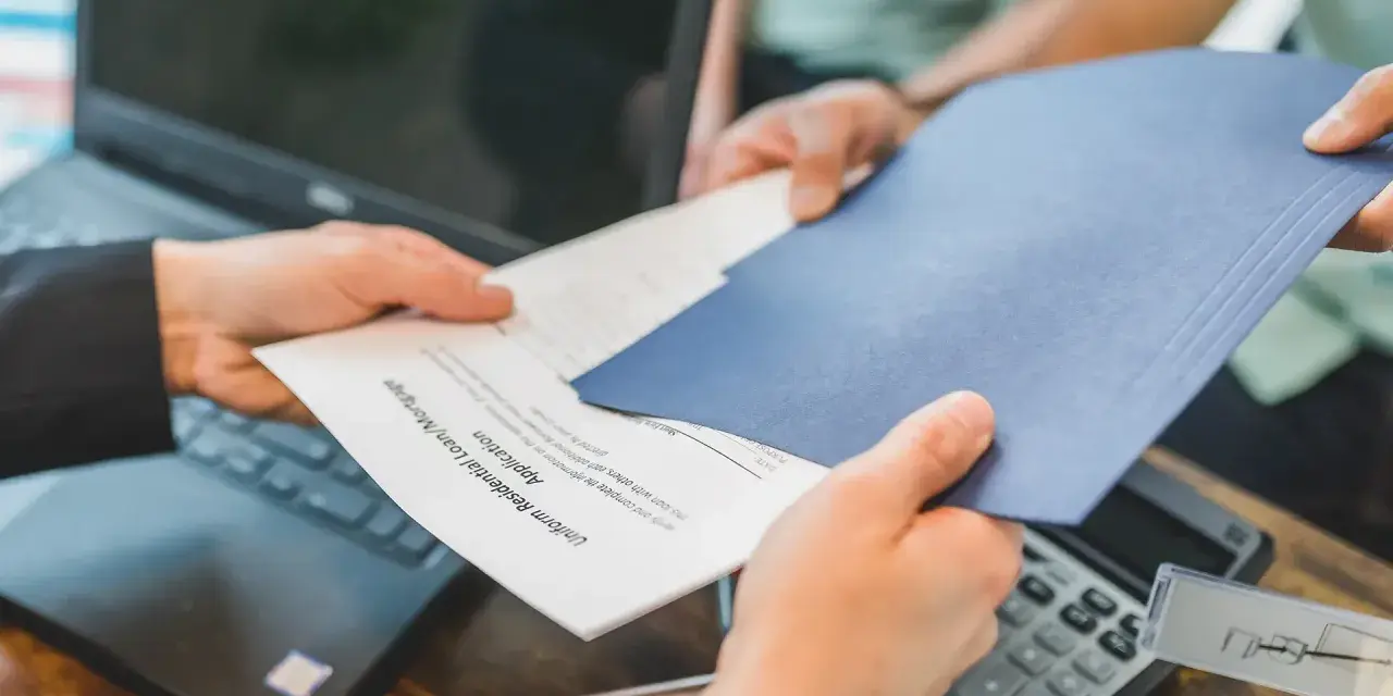 Des mains échangent des documents, un formulaire de prêt hypothécaire. La gestion de la durée de conservation des actes notariés est essentielle.