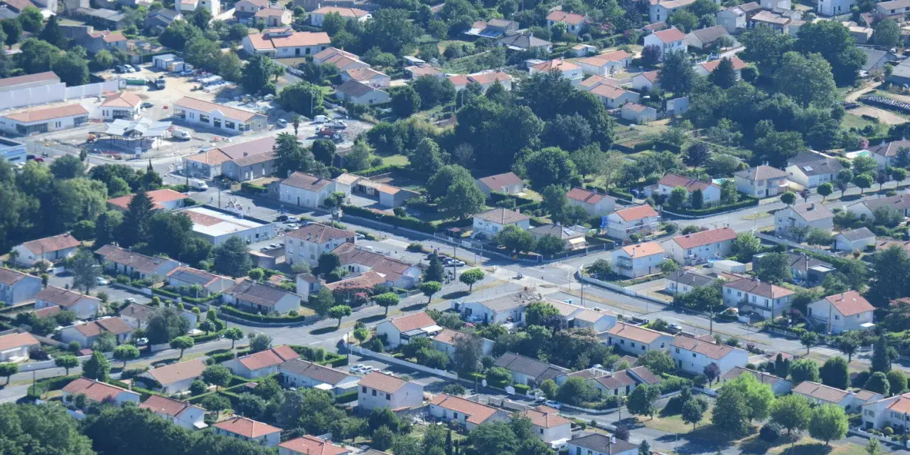 Vue aérienne d'un quartier résidentiel verdoyant, avec des maisons aux toits de tuiles rouges et des rues sinueuses. On aperçoit des chantiers, signe de développement, peut-être pour un nouveau plu à Niort.