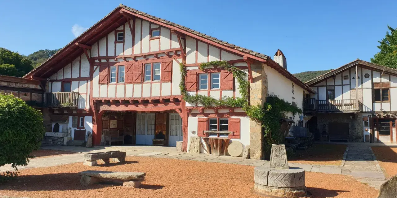 Maison basque traditionnelle à colombages rouges et blancs, avec un puits ancien devant. Un lieu plein de charme à Saint-Pée-sur-Nivelle.