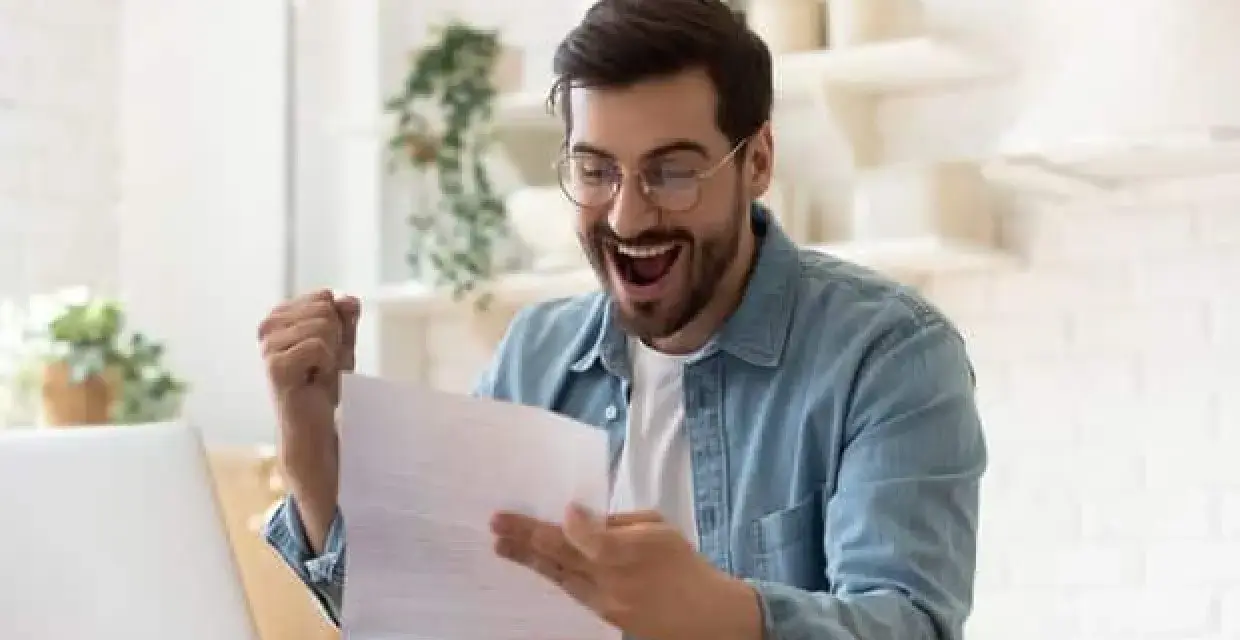 Homme joyeux, poing levé, découvrant une bonne nouvelle sur un document, peut-être la rémunération gérant SCI.