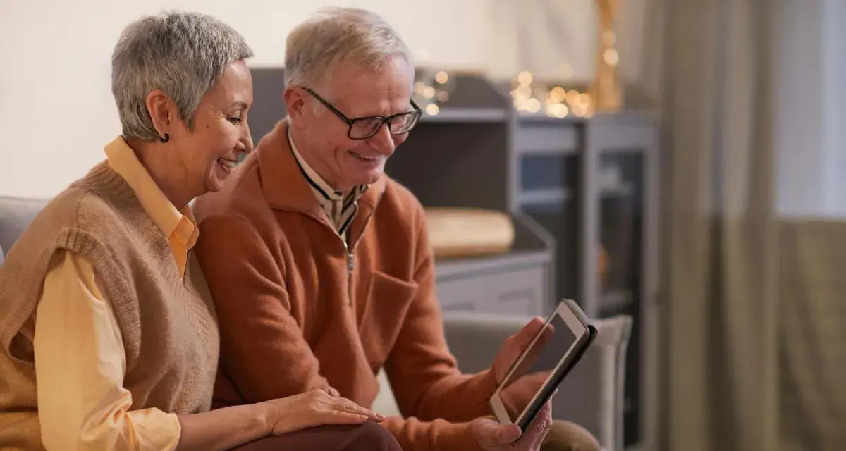 Un couple âgé regarde une tablette, peut-on louer un appartement après 70 ans ? Ils semblent heureux de leurs recherches.