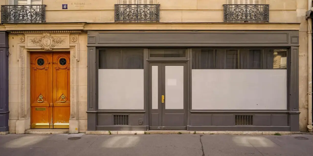 Une porte de commerce grise et une porte d'entrée en bois ornent cette façade parisienne.
