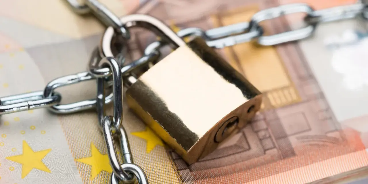 Un cadenas et une chaîne sécurisent des billets en euros, symbolisant la consignation de loyer ou la protection de fonds.