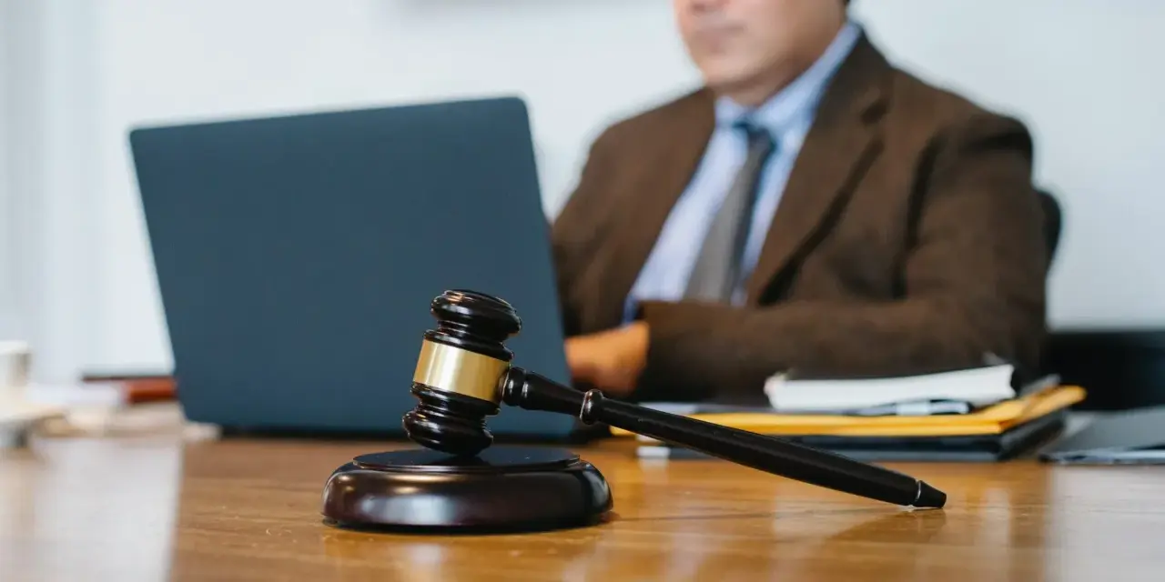 Marteau de juge sur un bureau, avec un homme en costume travaillant sur un ordinateur portable en arrière-plan. Explication de l'article 1722 du Code civil.