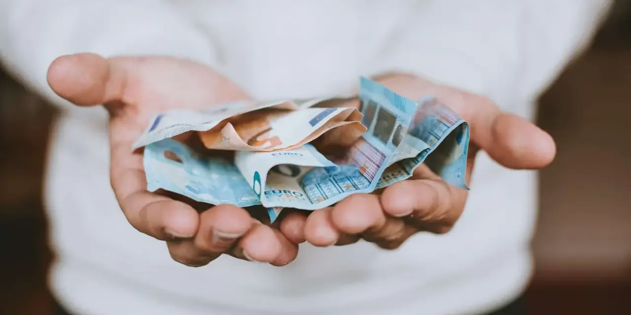 Mains tenant des billets en euros froissés, évoquant une transaction financière, peut-être une donation déguisée ou un viager.