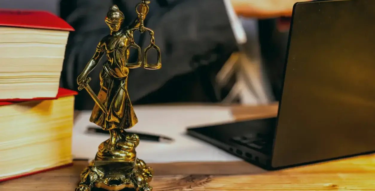 Statue de la justice, livres, ordinateur portable et stylo sur un bureau en bois. Un avocat examine les frais de donation.