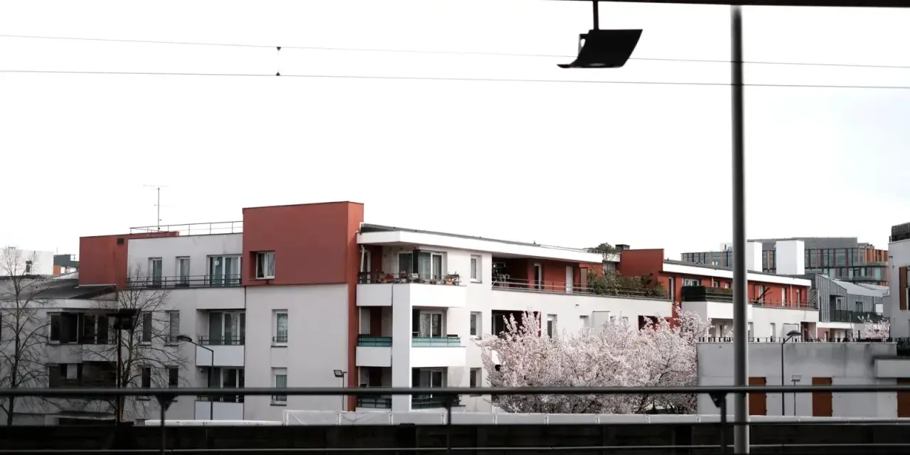 Immeubles modernes avec balcons fleuris, évoquant un **logement décent loi 1989**. Un cerisier en fleurs ajoute une touche printanière.