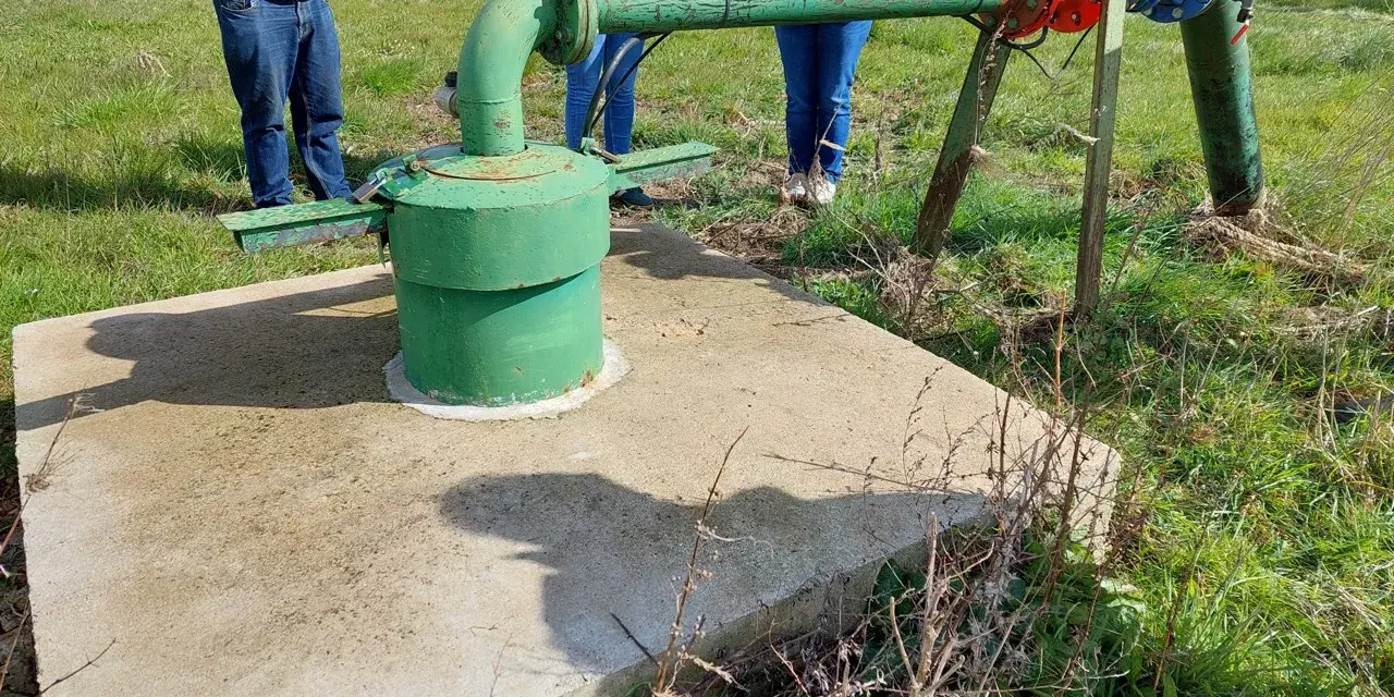 Installation de forage agricole, respectant la réglementation. Des personnes observent le système de pompage et de tuyauterie verte et bleue.