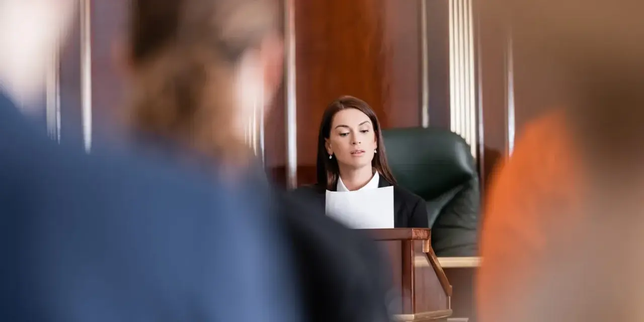 Une avocate présente son dossier, le dol, devant un juge. La salle d'audience est sombre et solennelle.