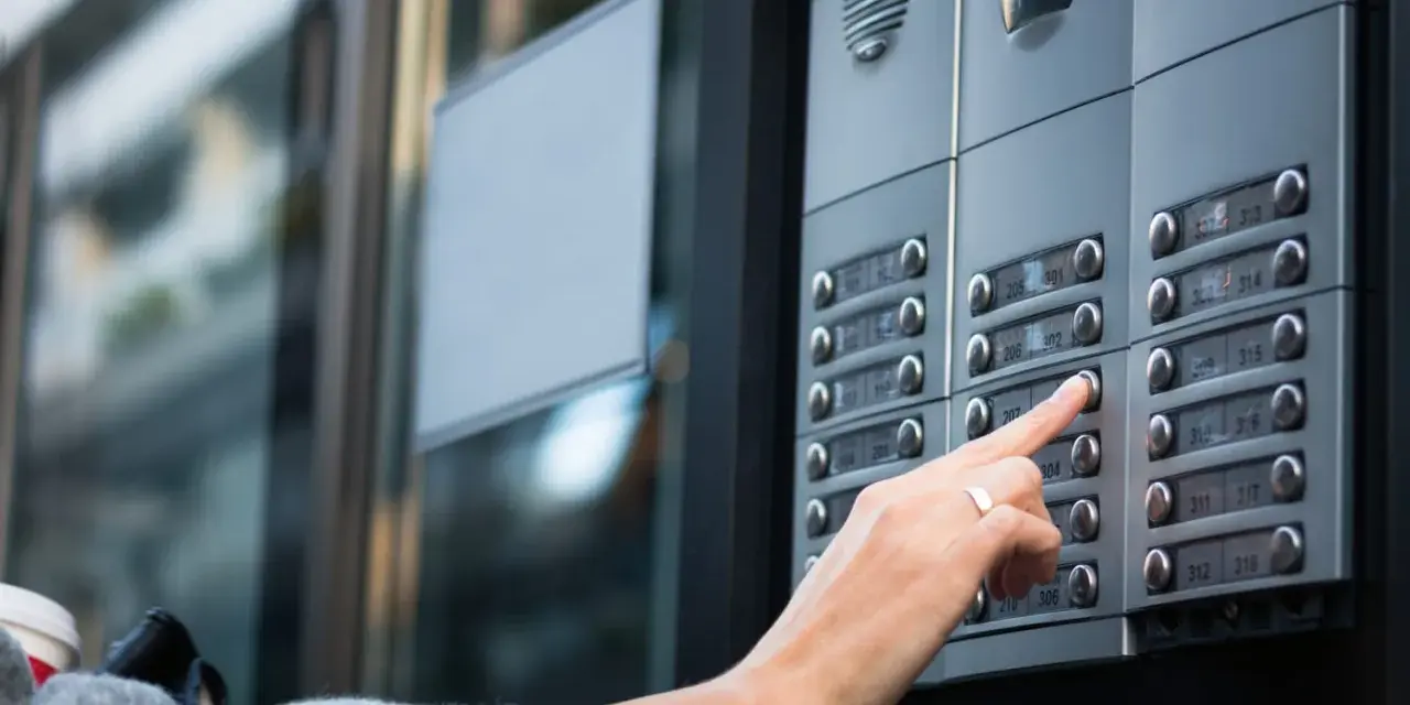 Une main appuie sur un bouton d'interphone, rappelant l'obligation du propriétaire d'assurer ce système.