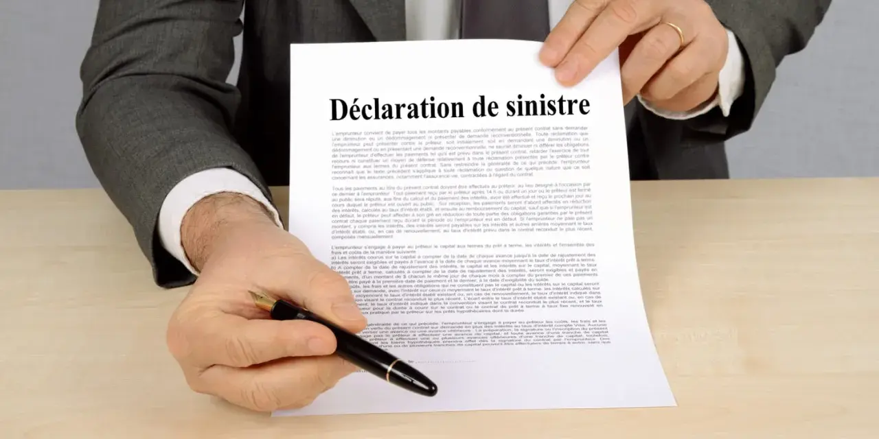 Un homme en costume gris tient un document intitulé "Déclaration de sinistre", prêt à signer.