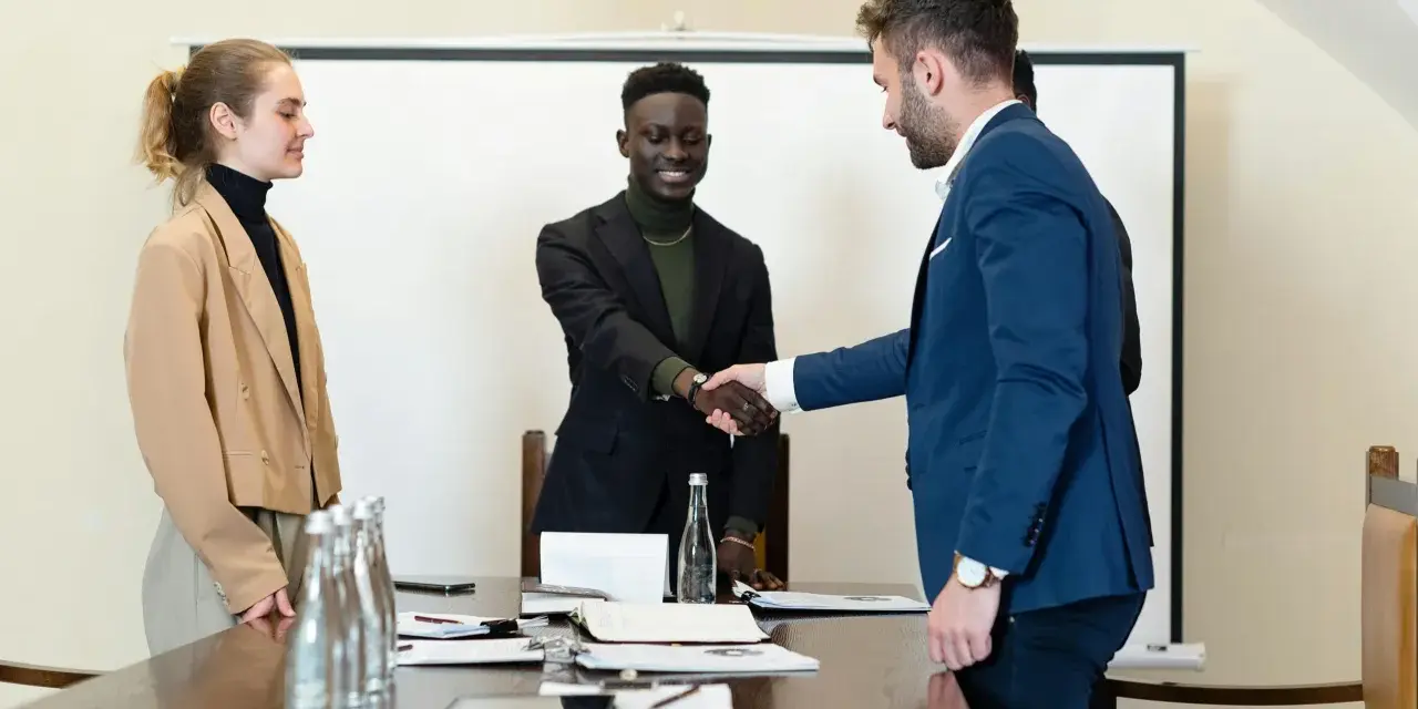 Trois personnes en tenue d'affaires se serrent la main. L'un d'eux discute des intérêts d'un compte séquestre notaire.