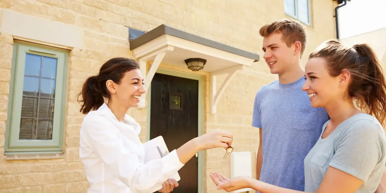 Une femme remet des clés à un jeune couple devant leur nouvelle maison. Le tableau droit de préemption locataire est respecté.