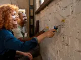 Un couple peint un mur en brique, résolvant un désaccord sur les travaux en indivision avec bonne humeur.