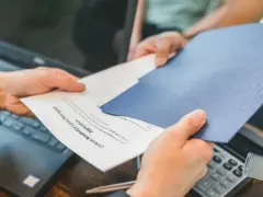 Des mains échangent des documents, un formulaire de prêt hypothécaire. La gestion de la durée de conservation des actes notariés est essentielle.