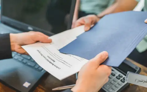 Des mains échangent des documents, un formulaire de prêt hypothécaire. La gestion de la durée de conservation des actes notariés est essentielle.