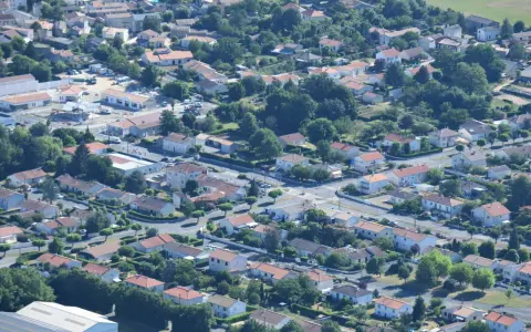 Vue aérienne d'un quartier résidentiel verdoyant, avec des maisons aux toits de tuiles rouges et des rues sinueuses. On aperçoit des chantiers, signe de développement, peut-être pour un nouveau plu à Niort.