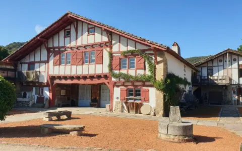 Maison basque traditionnelle à colombages rouges et blancs, avec un puits ancien devant. Un lieu plein de charme à Saint-Pée-sur-Nivelle.