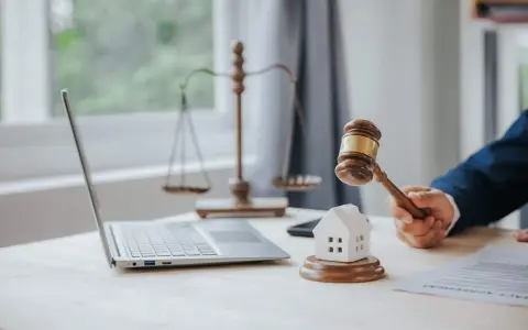 Marteau de juge frappant une maison miniature, symbolisant la loi Carrez pour une maison individuelle. Balance de la justice et ordinateur en arrière-plan.
