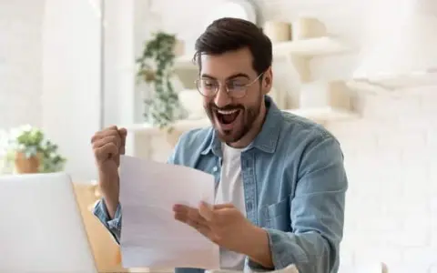 Homme joyeux, poing levé, découvrant une bonne nouvelle sur un document, peut-être la rémunération gérant SCI.