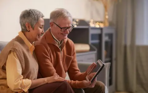Un couple âgé regarde une tablette, peut-on louer un appartement après 70 ans ? Ils semblent heureux de leurs recherches.